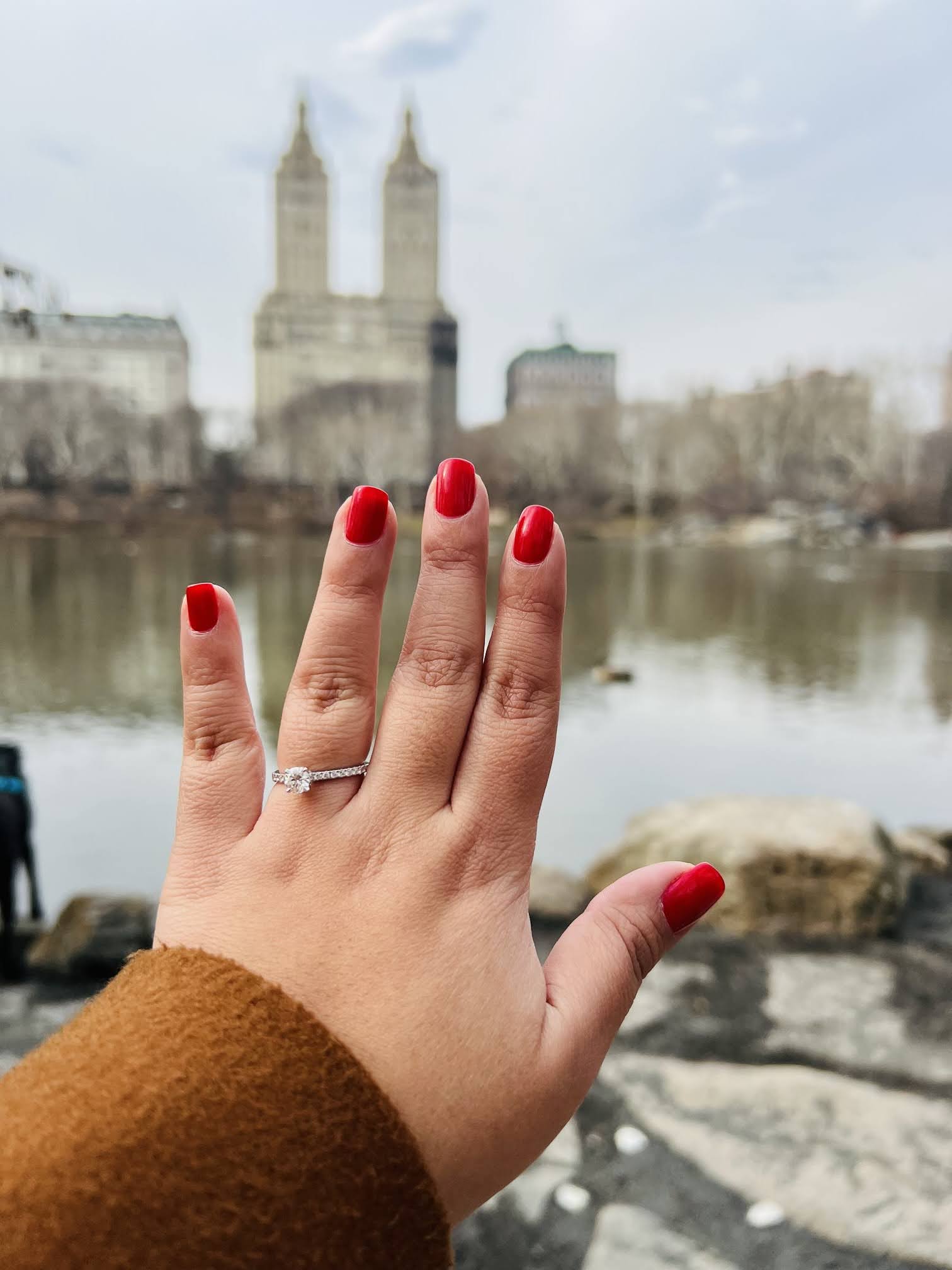 A person's hand with red nails and a city in the background