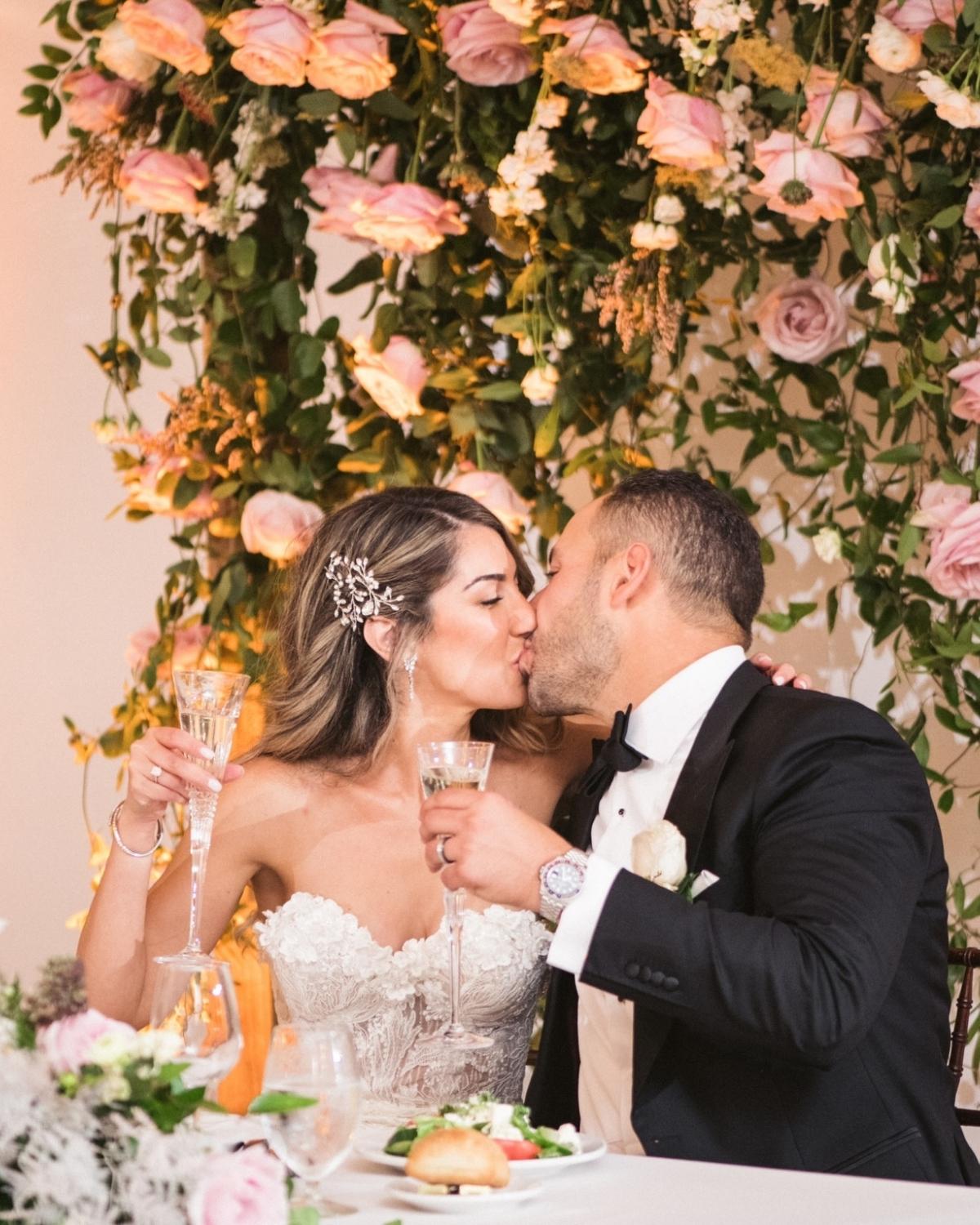 A couple at his wedding ceremony holding glasses of champagne. And kissing each other