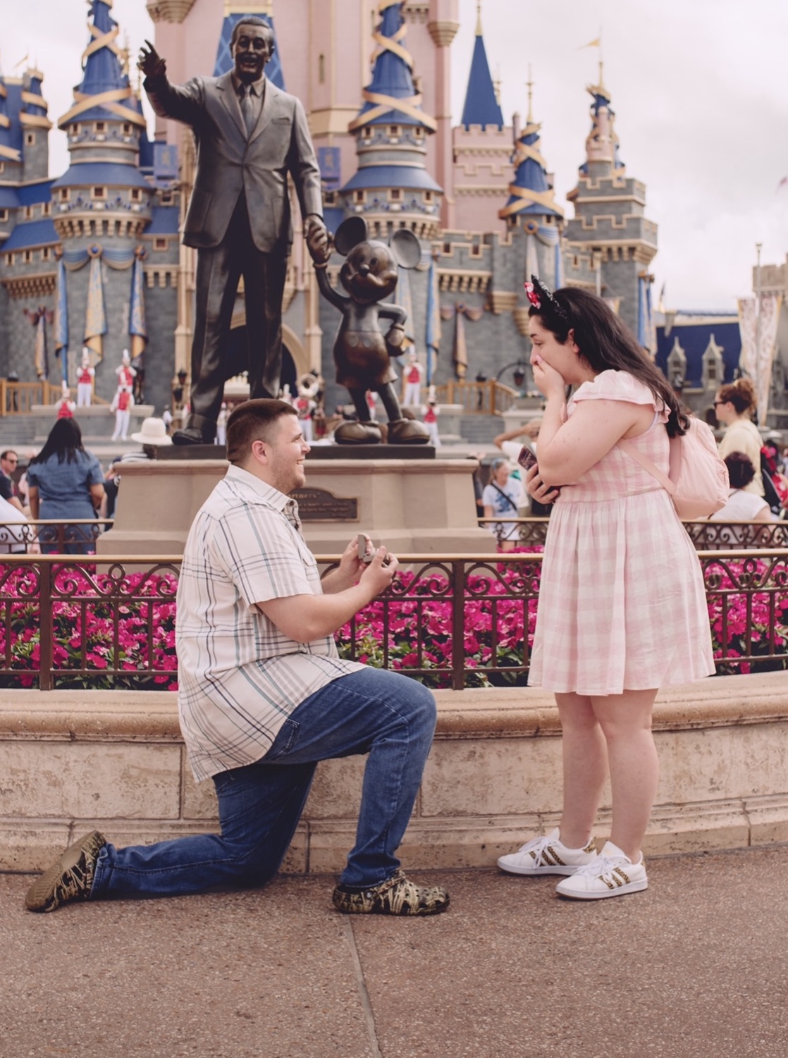 A boy proposing to a girl in front of the Walt Disney statue.